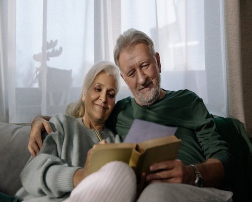 Happy senior Peruvian couple reading book together comfortably at home